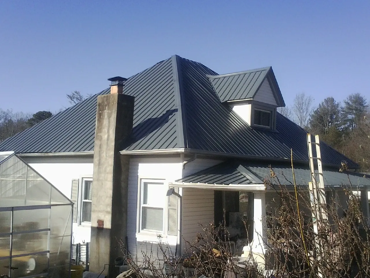 Dark blue standing seam metal roof on a white farmhouse with dormer — Slate & Tile Roof Repair by Roofing Brothers in Long Island