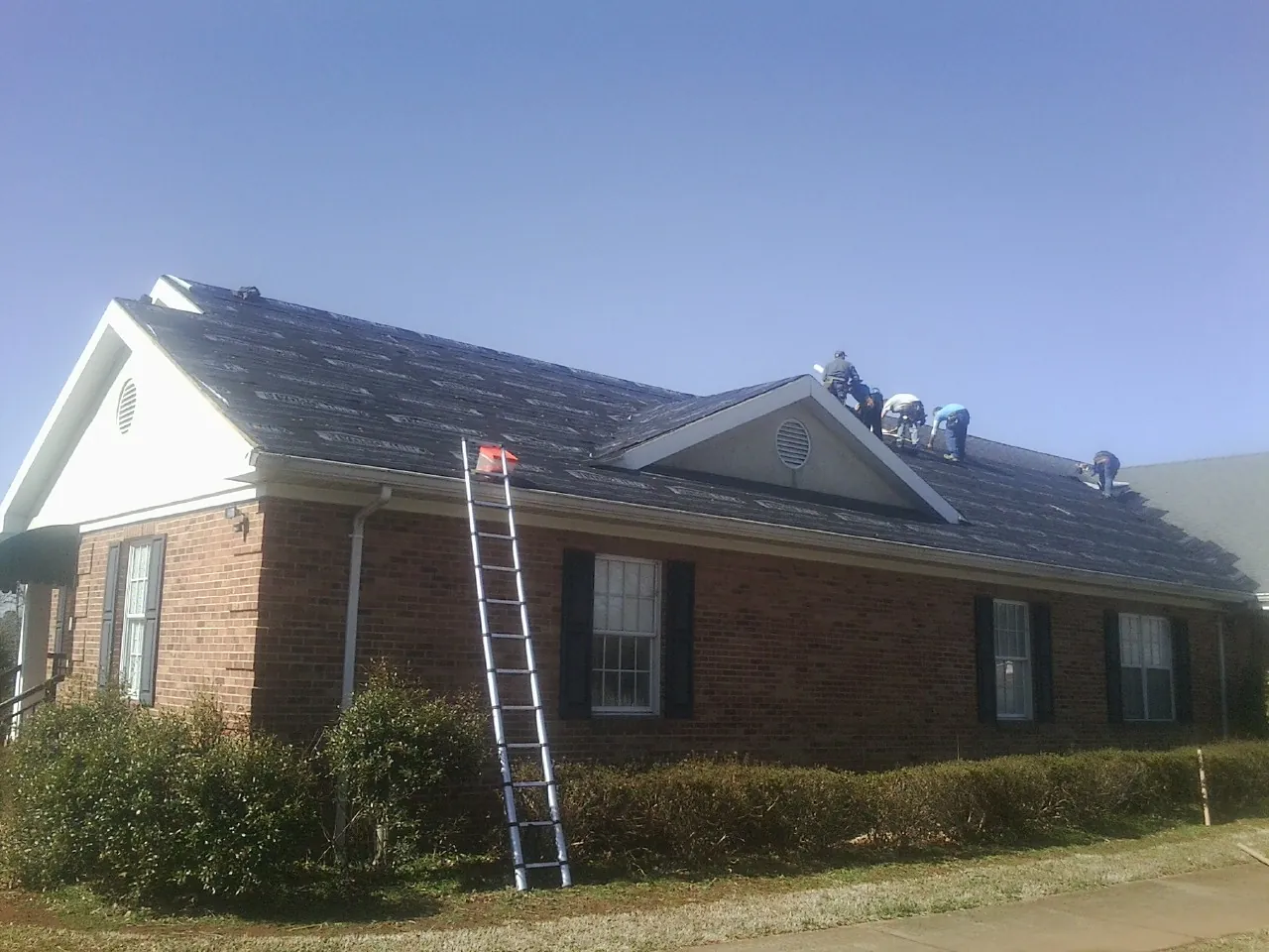 Crew tearing shingles off a brick ranch roof with a ladder set — Metal Roof Repair work by our crew in Long Island