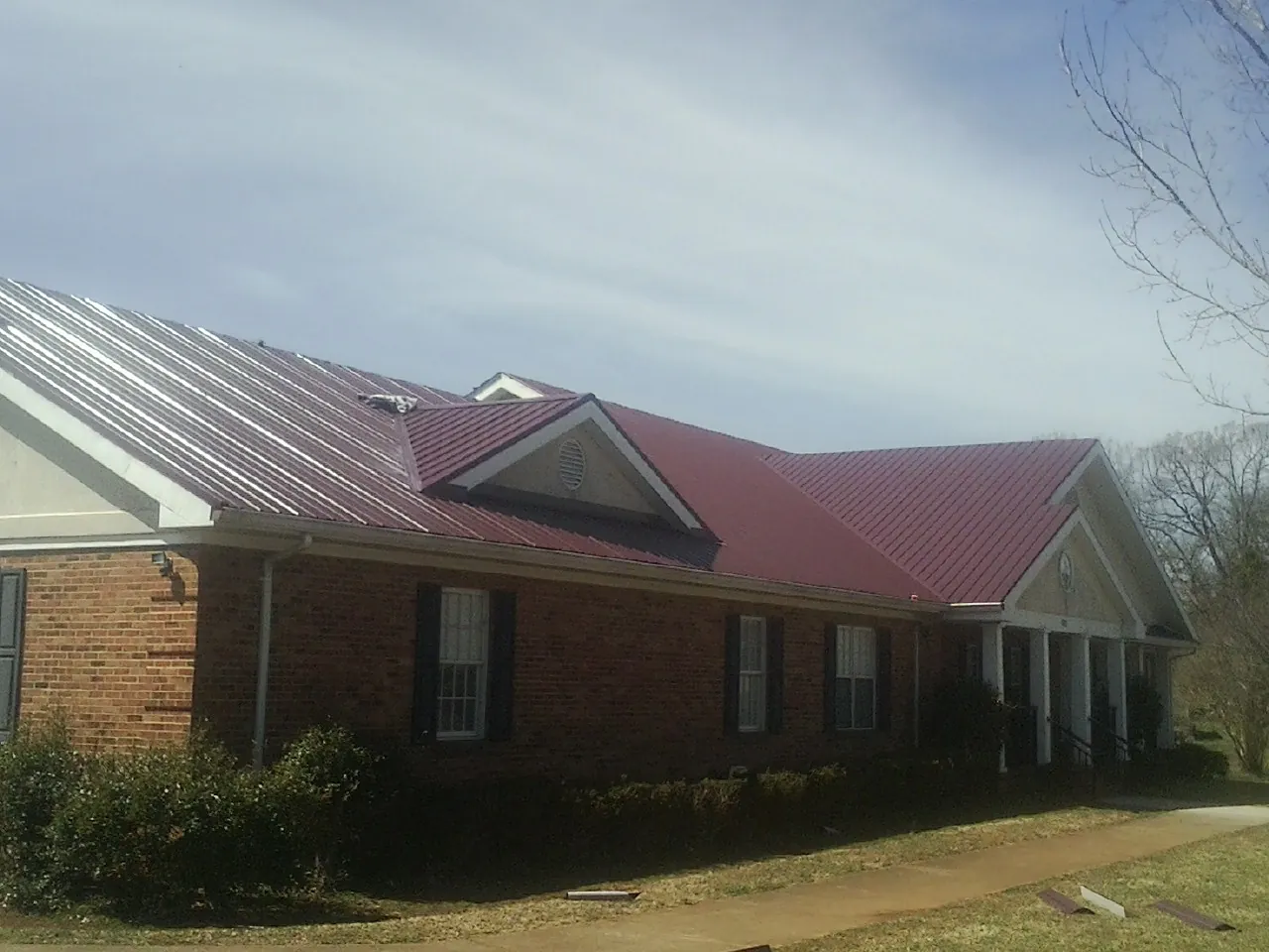 Red metal roof with gabled entries on a long brick building, from a Hail Damage Roof Repair job in Long Island