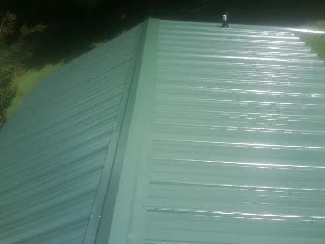 New green metal panels meeting at the ridge of a roof — Flat Roof Repair work by our crew in Long Island