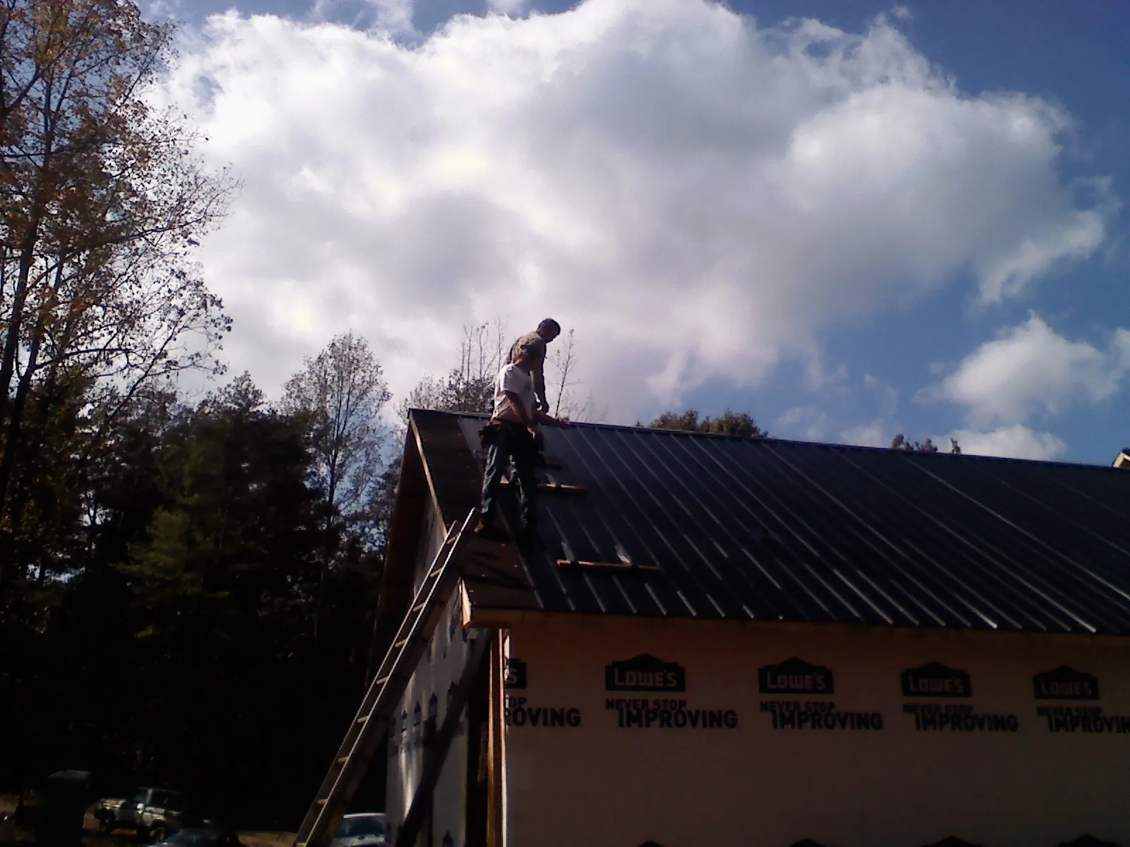 Roofer fastening dark metal panels high against a cloudy sky, from a Roof Inspection job in Long Island
