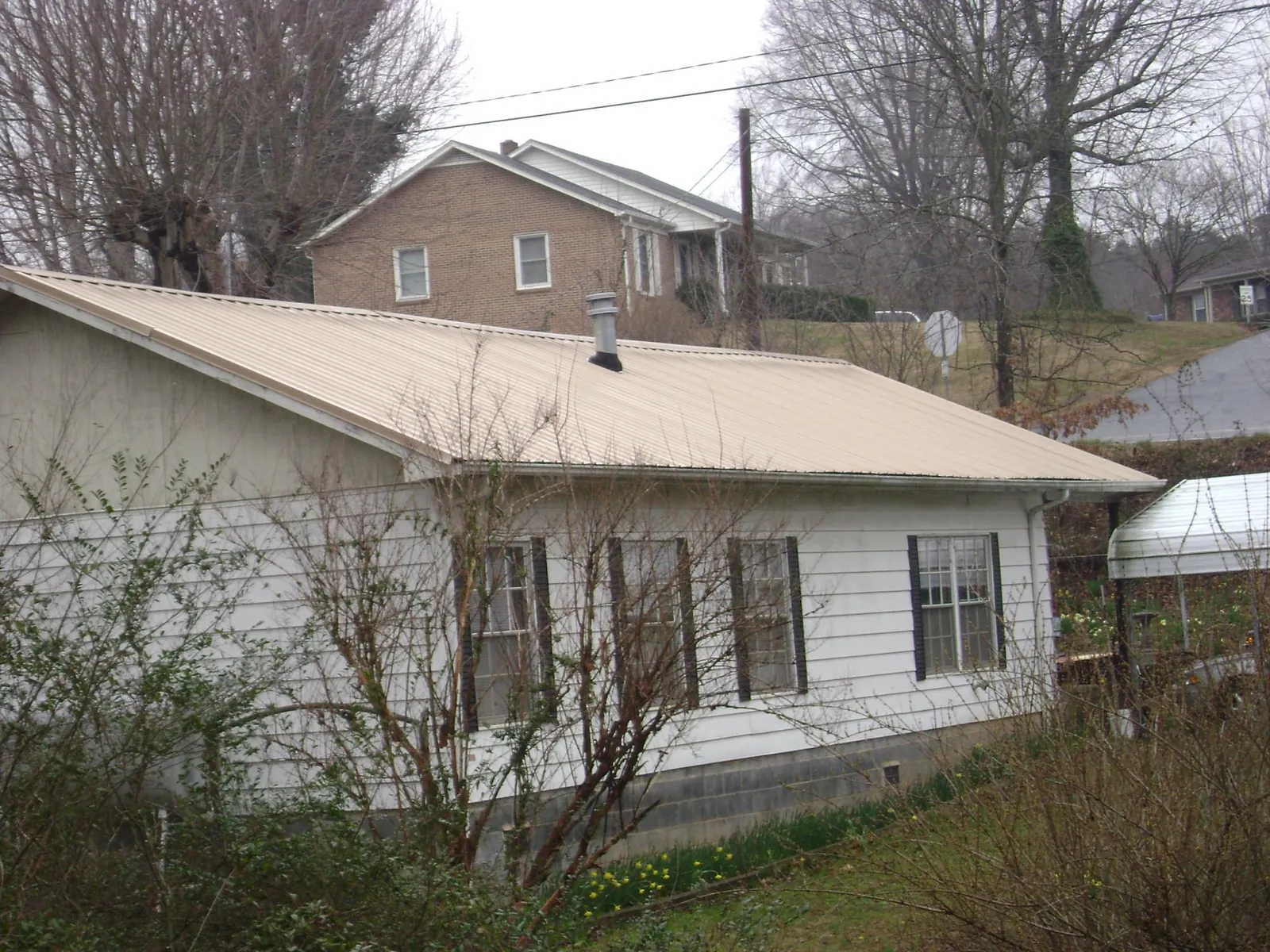 Tan metal roof on a white sided house set into a hillside — Commercial Roofing by Roofing Brothers in Long Island