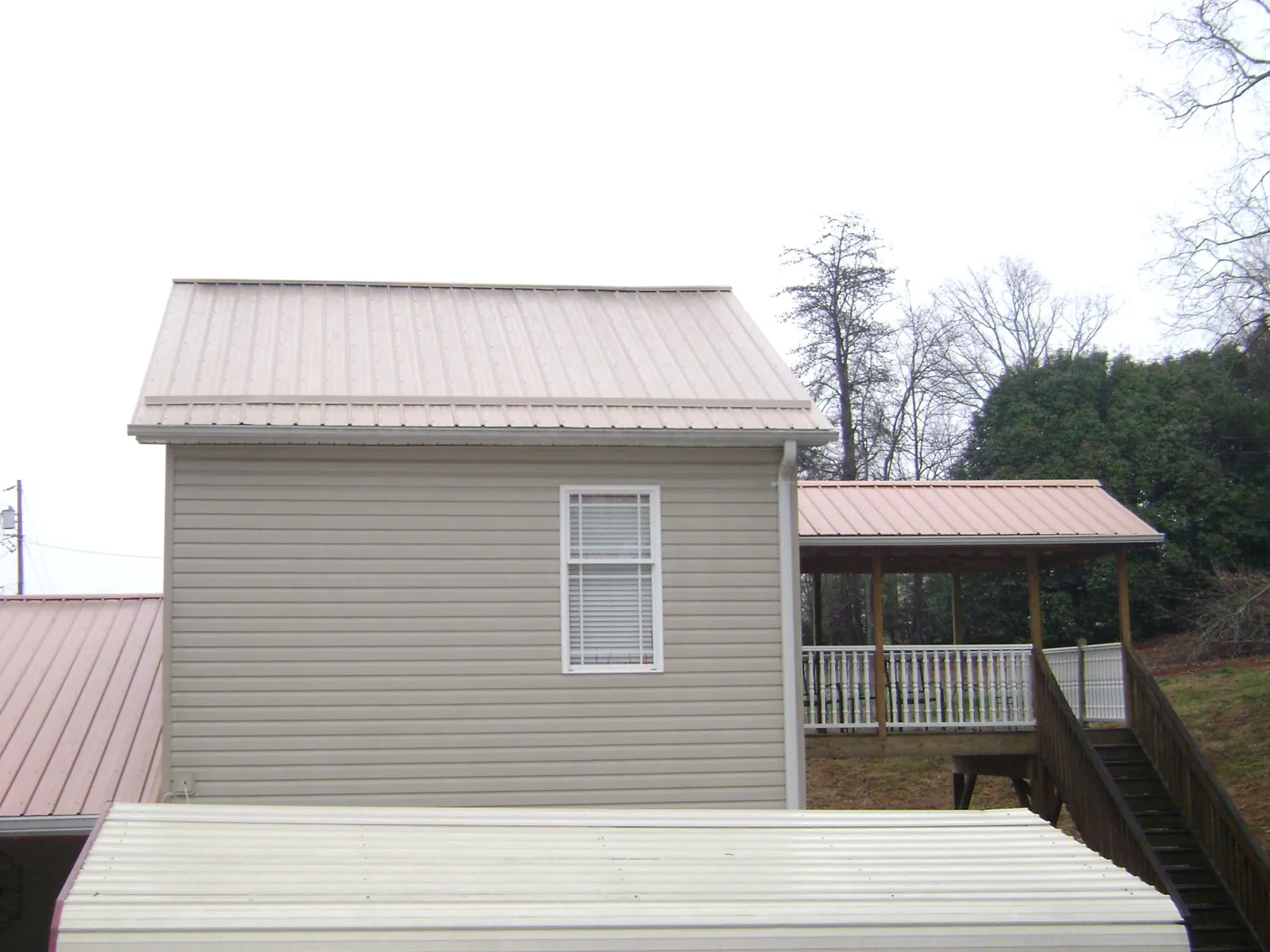 Tan metal roofs on a two story addition and attached porch, from a Roof Replacement job in Long Island